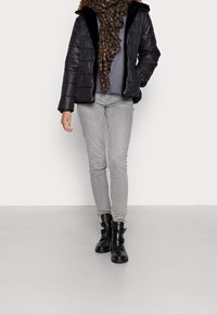 Černá péřová bunda s umělou kožešinou, šedý top, šedé přiléhavé džíny a černé kotníkové boty s páskovými detaily. Šála s leopardím vzorem.