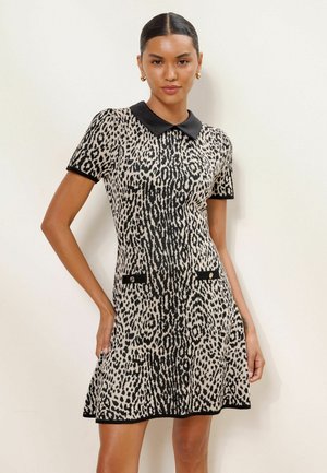 Frau trägt ein kurzärmeliges schwarz-weißes Kleid mit Animal-Print, schwarzem Kragen und dekorativen vorderen Taschen.