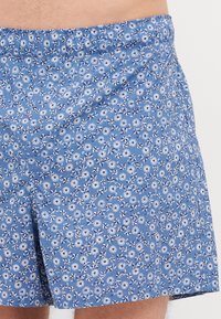 Blå blomstrede badebukser med lett stoff, elastisk midje og et gjentakende mønster av hvite og marineblå blomster.