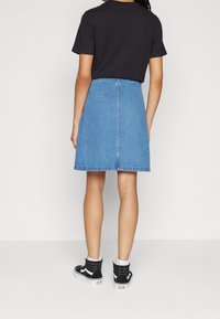 Denimkjol i ljusblått, knälång med en lätt A-linjeform, ihopparad med en svart kortärmad skjorta och svarta högskaftade sneakers.