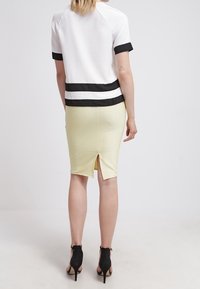 Haut à manches courtes blanc et noir avec un design rayé, associé à une jupe crayon jaune côtelée avec une fente arrière. Chaussures à talons hauts noires.