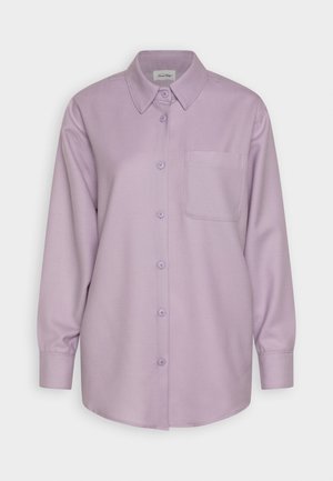 Lillā zīmuļš krekls ar garām piedurknēm, ar apkakli, vienu krūšu kabatu un mīkstu, gludu auduma struktūru. Pogas atbilst krekla krāsai.