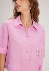 Maglietta rosa a maniche corte realizzata in tessuto testurizzato, con chiusura button-up, taschino sul petto con logo e colletto.