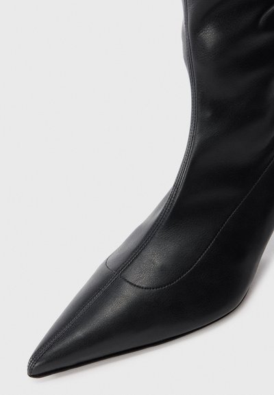 Cizma de gleznă din piele neagră, cu vârf ascuțit, textură netedă și detalii minime de cusătură. Design elegant, cu un aspect ajustat.