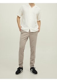 Witte korte mouw blouse met een relaxte kraag, gecombineerd met lichtbeige taps toelopende broek en zwarte sportieve sneakers.