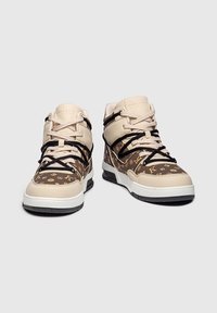 Zapatillas de baloncesto con un upper de cuero beige y marrón con un patrón de logo, cordones negros y una suela de goma blanca. Diseño de caña alta.
