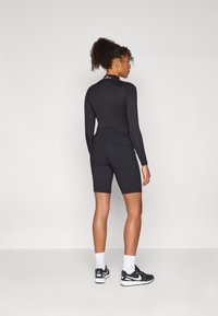 Svart langermet bodysuit med tettsittende design og høy krage, sammen med svarte sykkelshorts, brukt med svarte sneakers og hvite sokker.