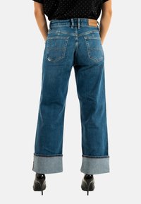 Jeans in denim blu a gamba larga con orli risvoltati e cuciture visibili. Presenta due tasche posteriori e un'etichetta con il marchio in vita.