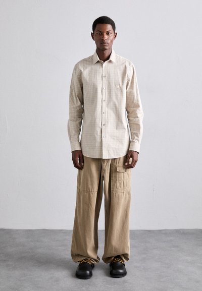 Beige rutigt skjort med lång ärm, matchat med lösa tanfärgade cargobyxor och svarta klumpiga skor med guldkedjeaccent.