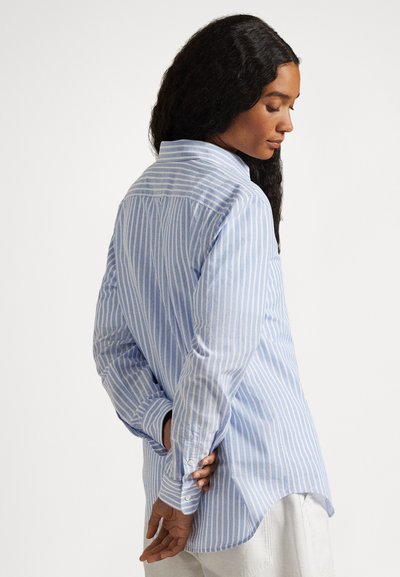 Μακρυμάνικο πουκάμισο με ανοιχτό μπλε και λευκές ρίγες, με γιακά με κουμπιά, στρογγυλεμένο τελείωμα και μανσέτες με κουμπιά. Το ύφασμα φαίνεται υφασμάτινο.