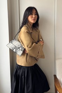 Šviesiai ruda tranšėja su plačiomis rankovėmis, juoda surinkta sijonas ir juodai-balta gyvatės odos rašto rankinė. Sklandžios tekstūros, modernus dizainas ir kontrastingos spalvos.