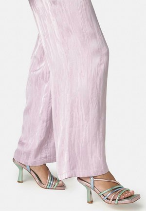 Gambe con pantaloni larghi a gamba larga in rosa chiaro con texture e sandali con tacco alto metallizzati pastello con multiple sottili cinturini.