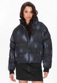 Gevulde zwarte jas met een glanzende afwerking, met een hoge kraag, rits aan de voorkant en een stervormige ritstrekkker. Subtiele blauwe accenten overal.