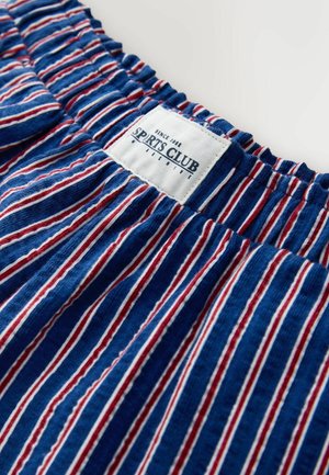 Raidallinen kangas sinisen, punaisen ja valkoisen sävyissä, jossa kootun joustinneuloksen kaula-aukko ja valkoinen etiketti, jossa lukee "SPORTS CLUB." Kangaspinta näyttää pehmeältä.