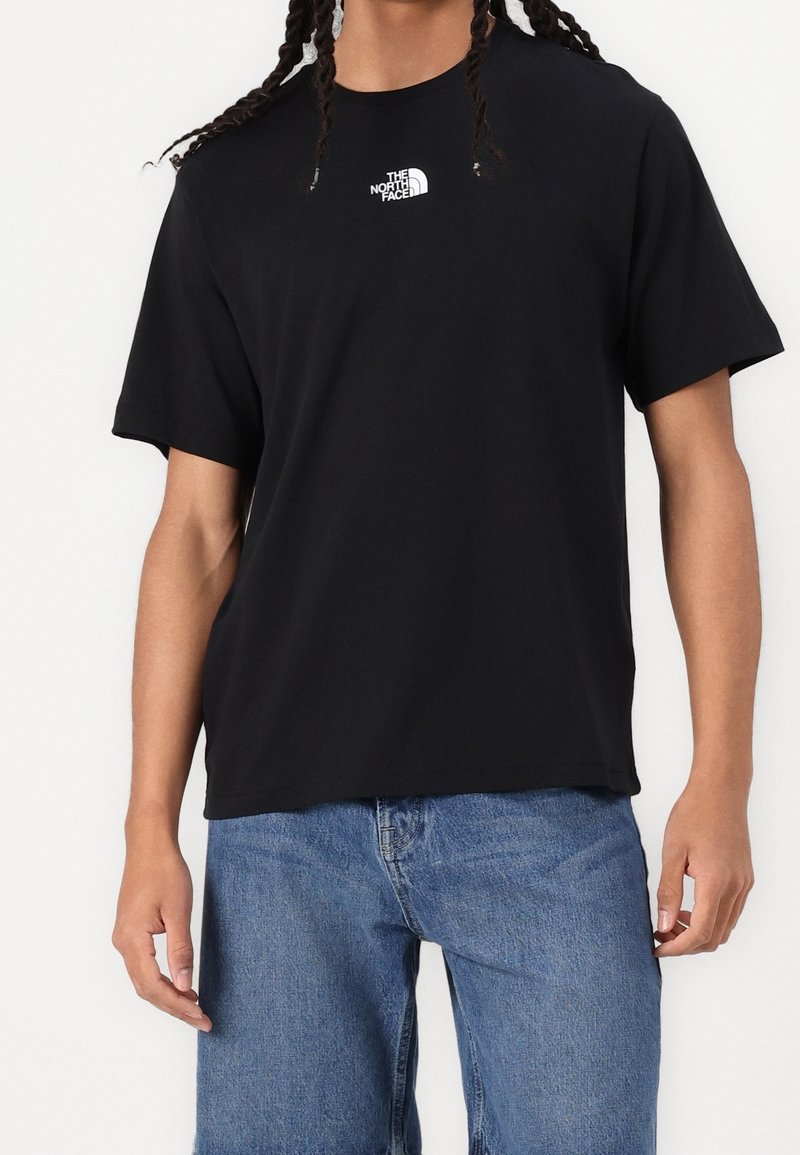 Camiseta de algodón negra con mangas cortas, que presenta un pequeño logotipo blanco en el pecho. La tela es suave y tiene un corte holgado.