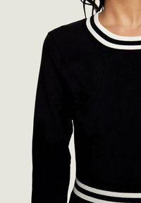 Pull noir côtelé à manches longues. Il présente un col rond rayé blanc et noir ainsi qu'un accent assorti à l'ourlet.