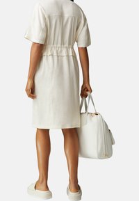 Abito corto color crema a maniche corte con vita arricciata, abbinato a una borsa bianca strutturata e scarpe slip-on strutturate. Design semplice e minimale.