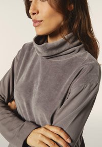 Suéter gris de cuello alto, confeccionado en una suave tela texturizada, con mangas largas y un corte relajado. Presenta detalles de costura sutiles.