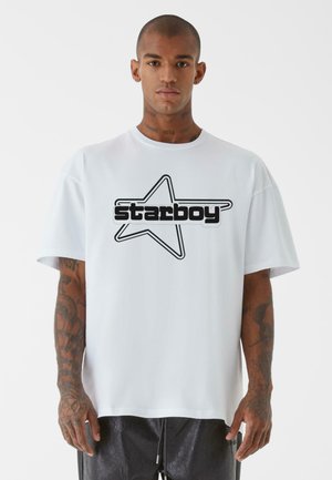 Hvit oversized t-skjorte med svart stjernesymbolikk og teksten "starboy", kortermet og med en avslappet passform. Mesh mykt bomullsmateriale.