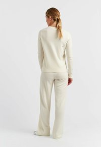 Licht crèmekleurige brei-trui en bijpassende broek. Bevat een ronde hals, lange mouwen en een subtiele logodetail op de achterkant van de trui.