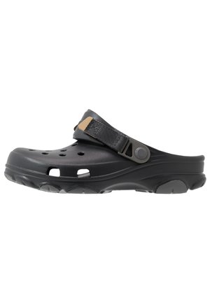 Zoccolo nero slip-on con fori di ventilazione e cinturino grigio regolabile sulla parte superiore, caratterizzato da una suola spessa e testurizzata per comfort e aderenza.