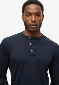 Navy langærmet henley skjorte lavet af bomuld, med rund halsudskæring, tre knaplukninger og minimalistisk design uden mønstre eller dekorationer.