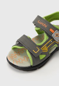 Grå barne sandaler med grønne detaljer, med to justerbare stropper, oransje mønstre på sålen og en strukturert overflate.