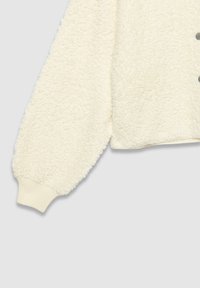 Veste en polaire couleur crème avec une surface texturée et duveteuse, manches surdimensionnées et poignets côtelés. Présente cinq boutons gris à l'avant.