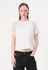 T-shirt bianco con maniche corte e trasparenti, scollatura rotonda e vestibilità rilassata, abbinato a jeans neri a vita alta. Design minimalista.
