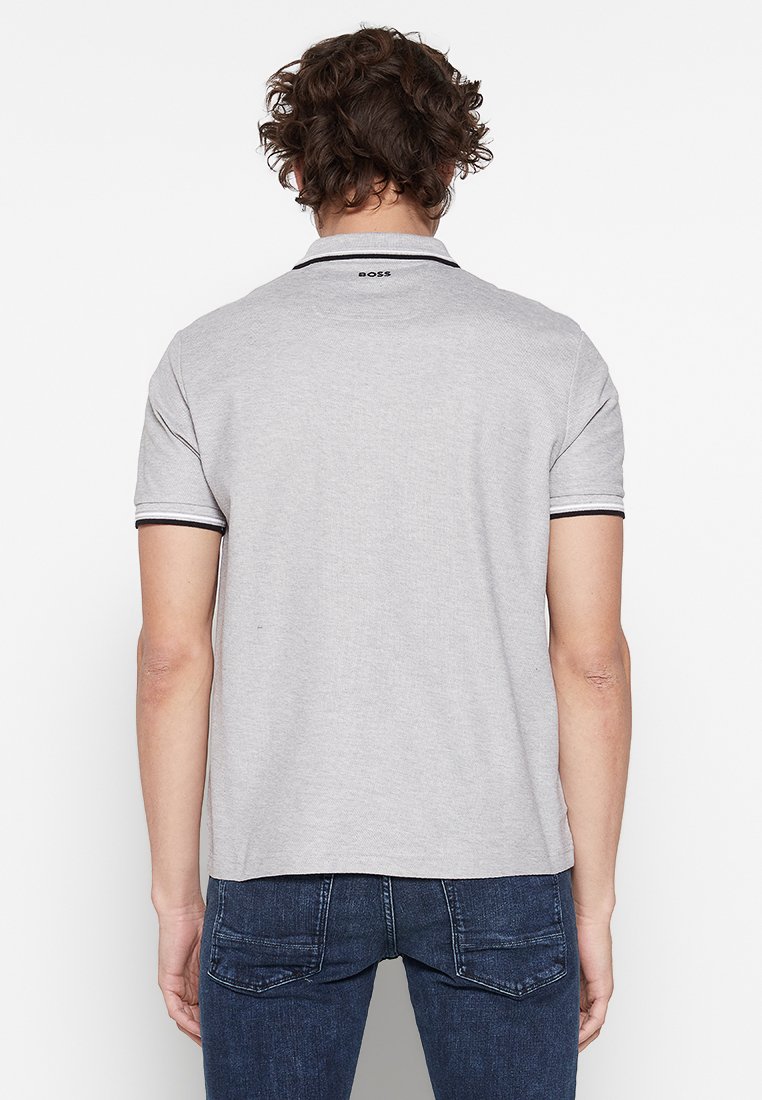 Grijze polo met donkere accenten op de kraag en mouwen, korte mouwen, en een logo op de bovenrug. Draag het met donkere denim jeans.