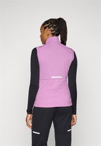 Vest purpuriu ușor cu guler înalt, material texturat și un model subtil pe spate. Asortat cu un top negru cu mânecă lungă.