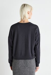 Mørkegrå, løs passform sweatshirt med rund hals og senkede skuldrer. Myk tekstur og avsluttet hemkant; brukt med et mønstrete grått skjørt.