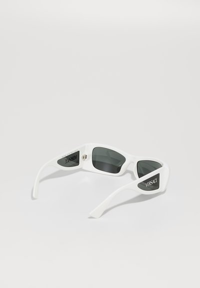 Lunettes de soleil blanches en plastique avec des verres gris foncé. Présentent une marque Versace sur la branche, une forme élégante et une finition brillante.