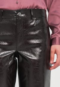 Hoge taille zwarte glanzende nepleer broek met een gladde textuur, voorzakken en een zilveren knoopsluiting.