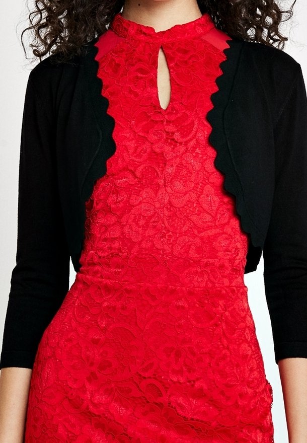 Rotes Spitzenkleid mit einem gewellten Ausschnitt und transparenten Akzenten, kombiniert mit einer enganliegenden schwarzen Strickjacke. Beide Teile haben angepasste Ärmel.