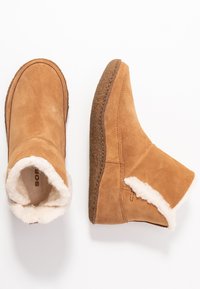 Tan-farbenen Wildleder-Stiefeletten mit weichem weißen Fellfutter und einer strukturierten braunen Gummisohle. Einfaches Nähen entlang der Seiten.