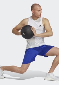 Adidas træningssæt bestående af en ærmeløs hvid top og blå shorts. Sort struktureret medicinbold med logo. Hvide sporty sko.