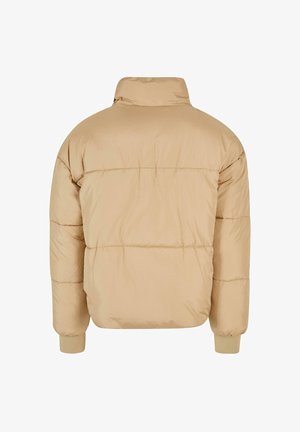 Beige puffer-takki korkealla kauluksella, tikattu muotoilu ja elastiset hihansuut. Sujuva pinta ja hieman yli-iso muoto.