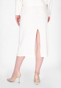 Valkoinen polvipituinen hame, jossa on sivureikä, valmistettu pehmeästä, teksturoidusta kankaasta. Yhdistettynä nude-sävyisiin korkokenkiin. Minimalistiset design-yksityiskohdat.