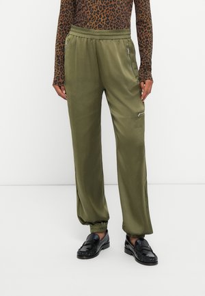 Pantalones jogger de satén verde oliva con cintura elástica y bolsillos con cremallera en los costados, combinados con una blusa de manga larga de estampado de leopardo marrón.