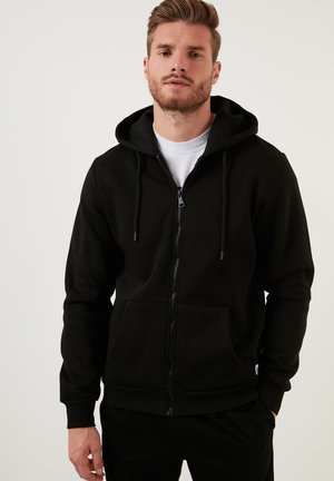 Black zip-up hoodie made of soft fabric, featuring a front pocket, drawstring hood, and ribbed cuffs. Simple design, no patterns or accents.