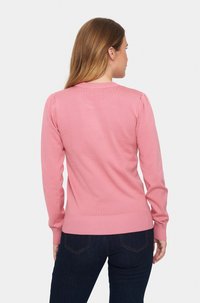 Ljusrosa tröja med ribbad halsringning och muddar, med en figurnära silhuett. Tyget verkar mjukt med en jämn textur.