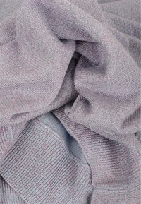 Tissu tricoté doux de couleur violet clair avec des fils métalliques subtils, montrant des plis et une texture côtelée en vue rapprochée.