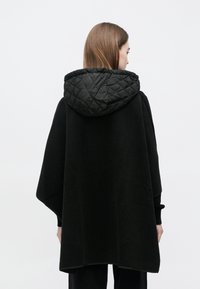 Mustast materjalist pončo, millel on must tikanditega kapuuts ning pehme tekstuur. Disain on lai ja voogav, katab keha ning sellel on minimaalsed metalldetailid.