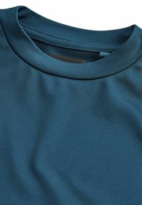 Teal träningsskjorta med en mjuk, elastisk tyg, rund halsringning och utan synliga mönster eller detaljer.