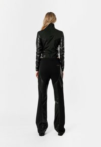 Chaqueta negra con mangas de cuero, cierre de cremallera y cuello alto, combinada con pantalones negros de pierna ancha que cuentan con detalles de cuero y texturas.