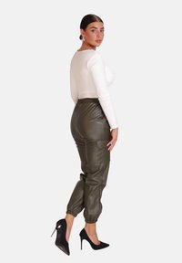 Witte lange mouw top gecombineerd met groene neplederen joggers, met een elastische tailleband en manchetten. Model draagt zwarte stilettohakken.