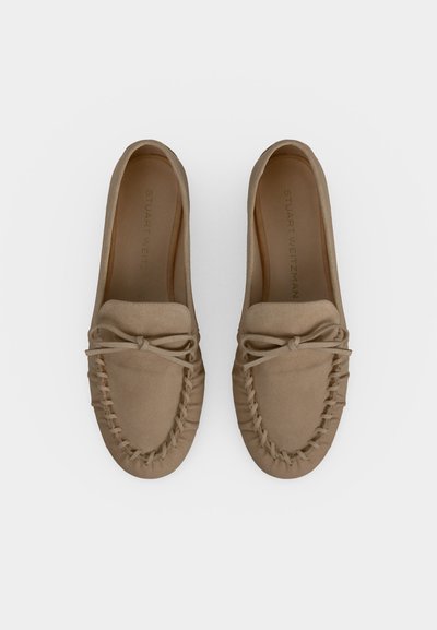 Paire de mocassins beige en daim avec des détails cousus et des accents en forme de nœud, vus de dessus sur fond blanc.