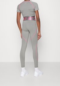 Šedý sportovní top a legíny s růžovými detaily a prošitím. Legíny mají vysoký pas a oba kusy jsou těsně přiléhavé.