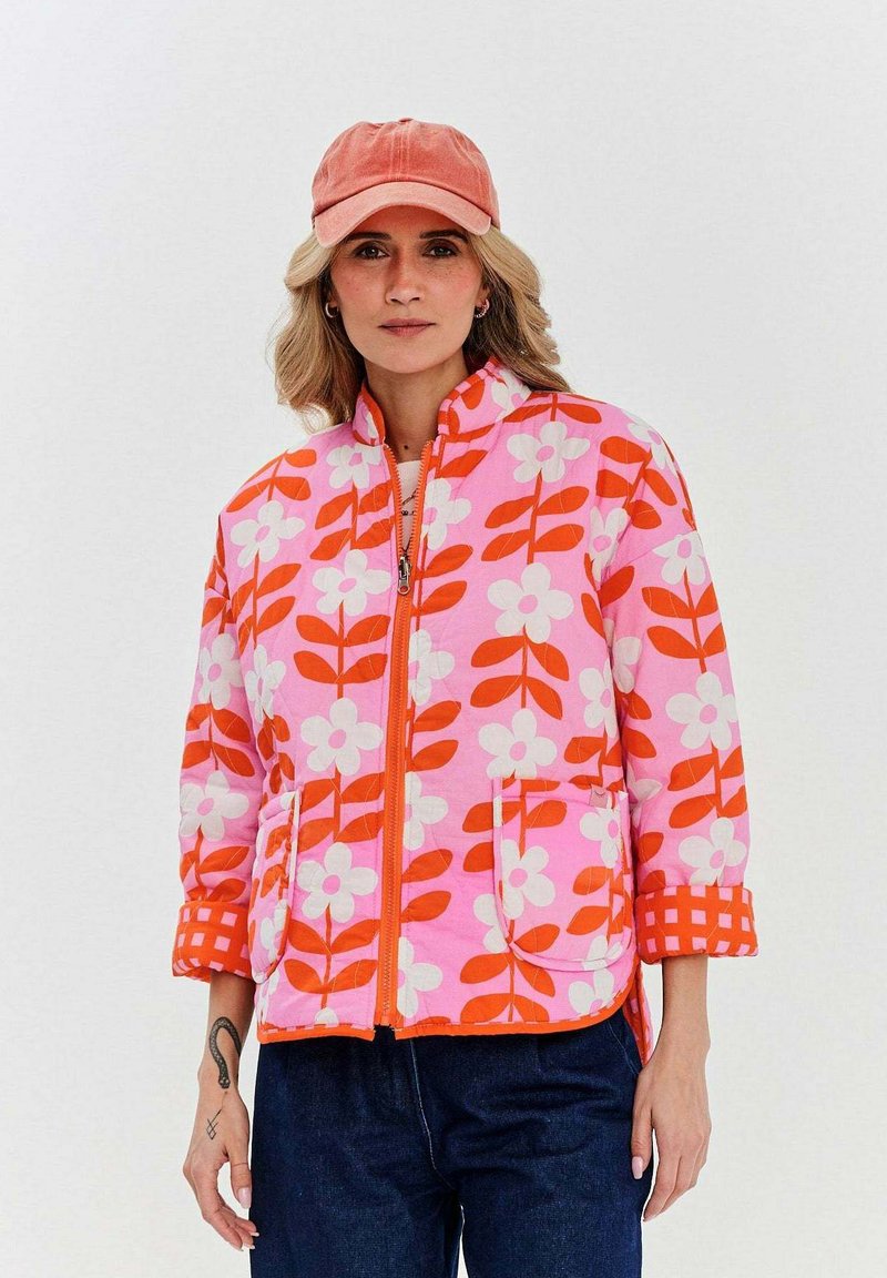 Ružová bunda s kvetinovým vzorom a červenými a bielymi kvetmi, so zipsom a dvoma náprsnými vreckami, doplnená korálovou čiapkou.